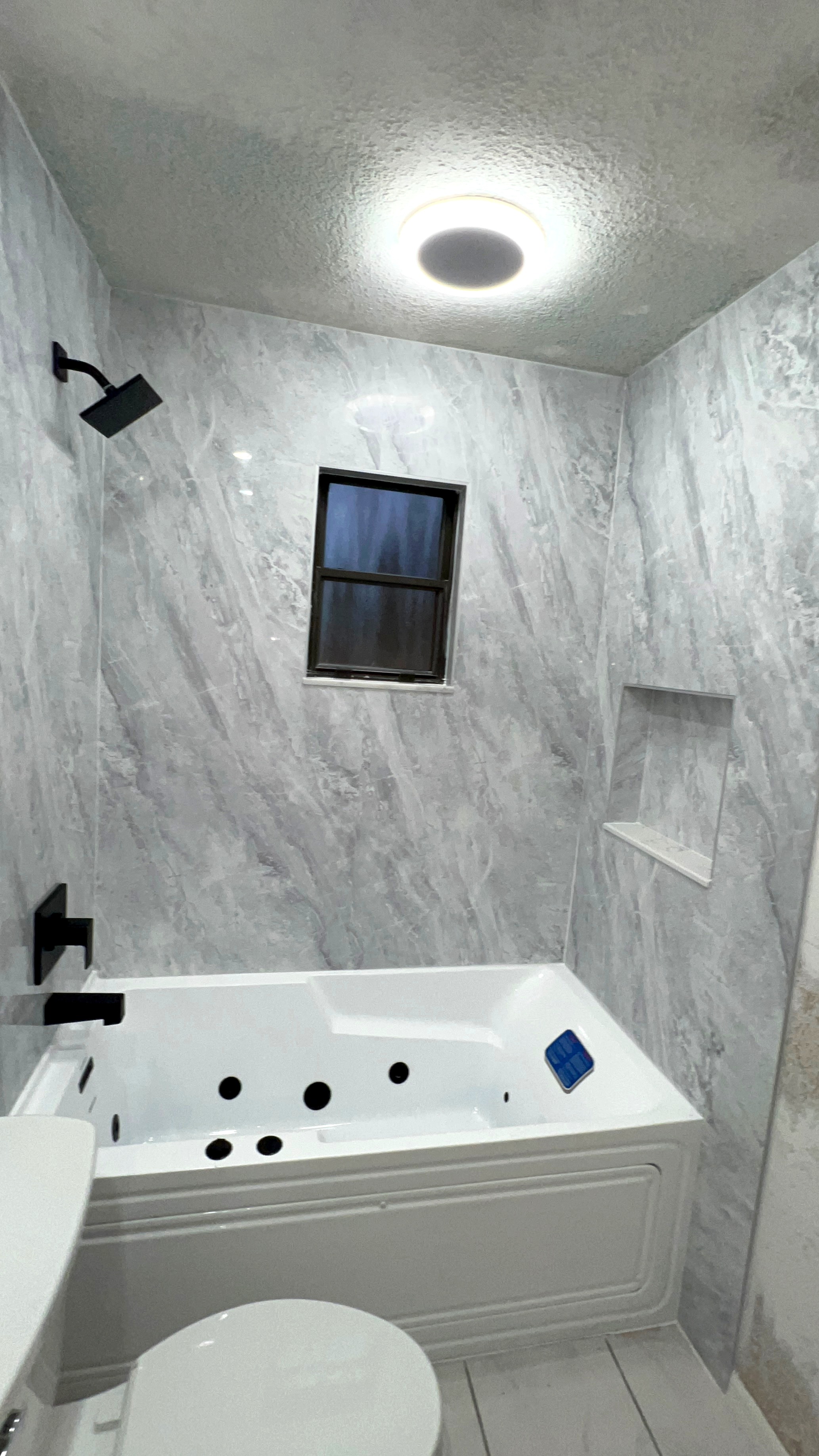 Marble surround jetted tub with matte black fixtures and recessed niche